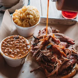 a pulled pork sandwich with beans and coleslaw