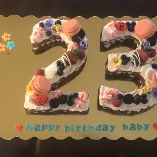 Chocolate cookie letter cake decorated with macarons, fresh fruit, fondant flowers, candies and meringue kisses