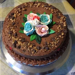 Chocolate Mousse cake with chocolate buttercream frosting and garnished with toasted nuts and chocolate chunks. Fondant flower decoration.