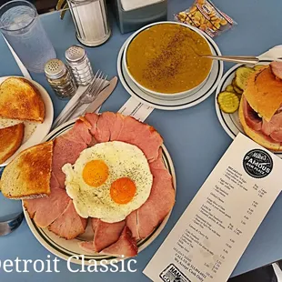 a plate of ham, a bowl of soup, and a sandwich