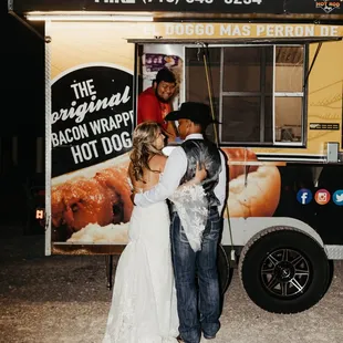 a bride and groom kissing in front of a hot dog truck