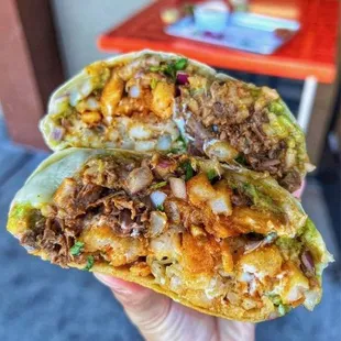 Cali Burrito stuffed with beef birria, french fries, cheese, rice, beans,  cilantro, onions, guacamole, sour cream