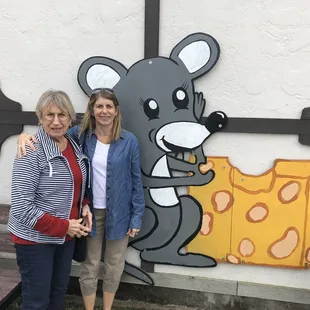 two women standing in front of a mural of a mouse