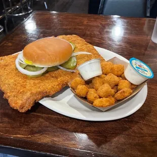 a fried chicken sandwich with pickles and tater tots