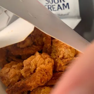 a hand holding a box of fried chicken