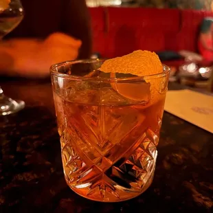a glass of cocktail with a orange garnish