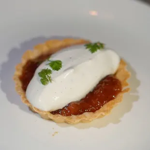 a white plate with a small pie topped with sour cream and garnished with parsley