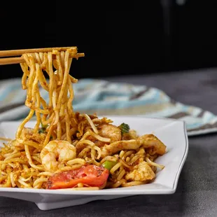 a person holding chopsticks over a plate of noodles