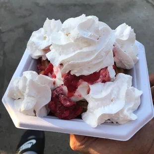 a hand holding a container of ice cream and strawberries