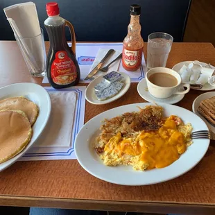 a breakfast of eggs, pancakes, hash browns, and coffee
