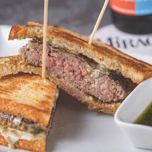 a grilled beef sandwich with a side of pesto sauce