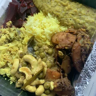 Dinner plate - lots of curries, veggies, around yellow rice and served on banana leaves
