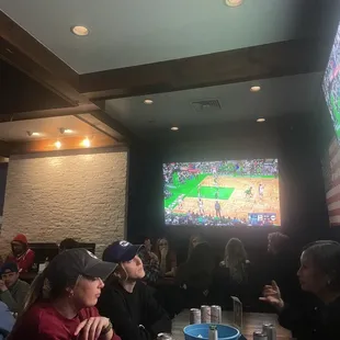 a group of people sitting at a table watching a baseball game