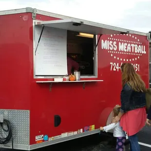a red food truck with people standing in front of it