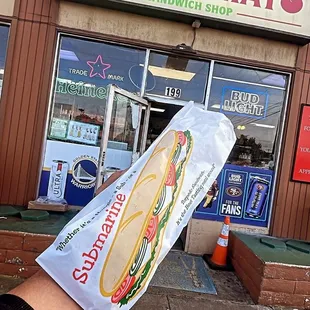 a person holding a sandwich in front of a store