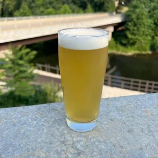 a glass of beer on a ledge overlooking a bridge