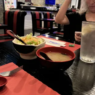 a woman sitting at a table with a bowl of soup and a glass of water