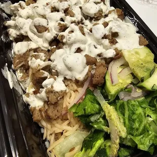 Gyro bowl drizzles with white sauce, and a side of salad with green sauce.