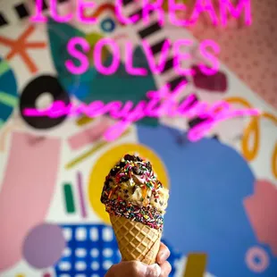 a hand holding an ice cream cone with sprinkles