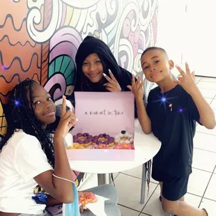 three girls sitting at a table with a sign