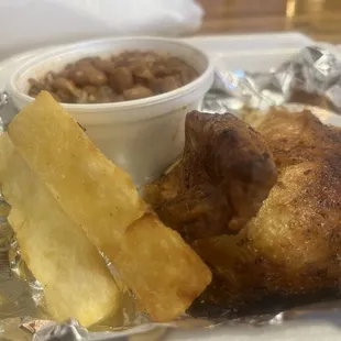 A quarter white chicken with pinto bean sauce and rice and yucca fries