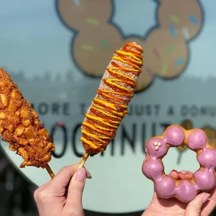 a person holding a donut and a fried chicken on a stick