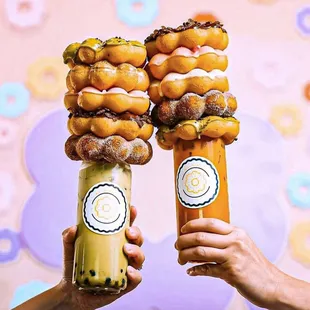 two people holding up two tall donuts