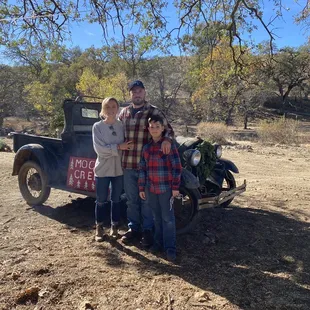 My daughter, her fiancé, and his son pose in front of the old car.