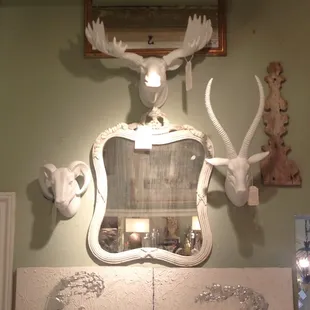 Antique French carved mirror surrounded by modern white faux animal mounts .