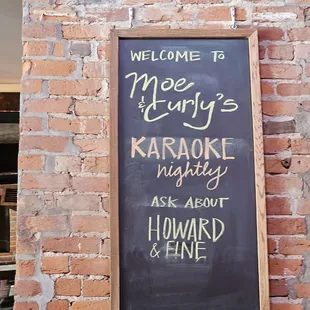 a chalkboard with the words welcome to mary&apos;s karaoke in front of a brick wall