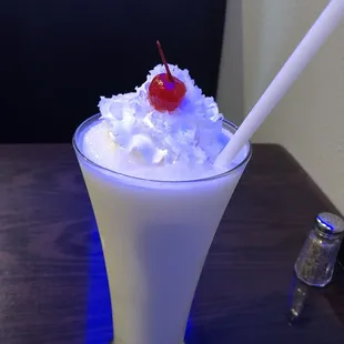 a glass of milkshake with a cherry on top