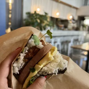 a hand holding a sandwich with rice and sausage