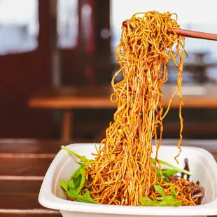 a woman holding chopsticks over a bowl of noodles