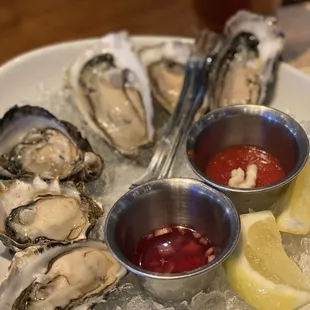 a plate of oysters with ketchup and lemon wedges