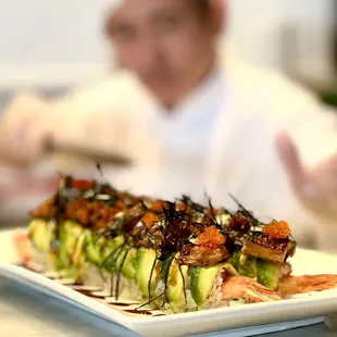 a man in a chef's uniform behind a plate of sushi