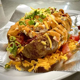 Our Yard Bird Baked Potato comes with butter, sour cream, tomatoes, chopped bacon, chopped chicken, cheese, chipotle aioli and green onions.