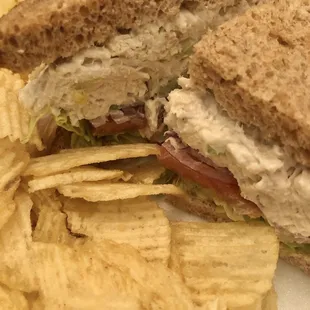 Chicken salad sandwich on wheat with lettuce, tomatoes, onions and chips on the side.