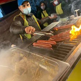 a man cooking hot dogs on a grill