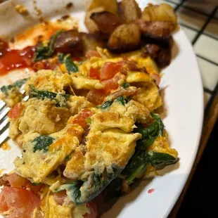 An already started to be eaten tomato, cheddar cheese, spinach and bacon scramble.