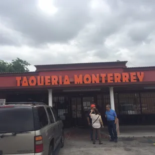 two people standing in front of a taqueria