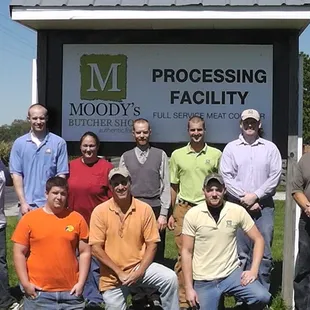 a group of men posing in front of a sign