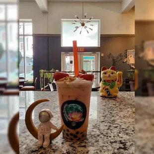 a cup of bubble tea with a cat figurine in the background