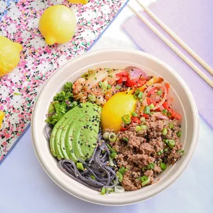 a bowl of food with noodles, meat, avocado, and lemons