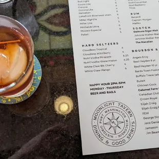 This is a picture of a drink, a Manhattan on the left and a menu on the right showing the Moonlight Tavern's liquors.