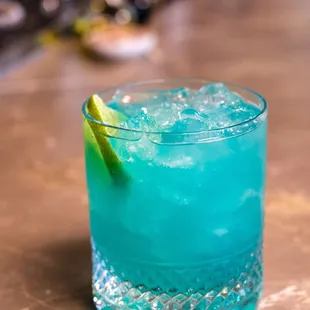 a blue cocktail with a lime slice