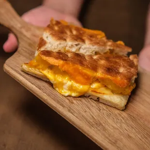 a person holding a wooden board with a sandwich on it