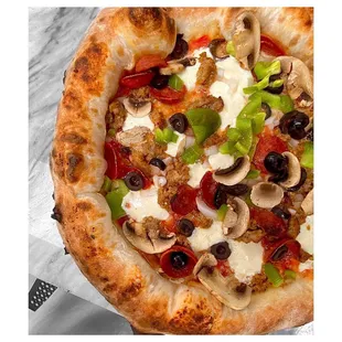 a pizza with mushrooms, peppers, olives, and cheese
