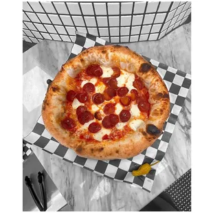 a pepperoni pizza on a checkered plate