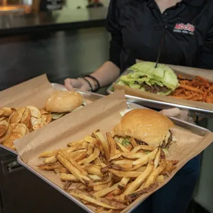 a woman holding two trays of burgers and fries