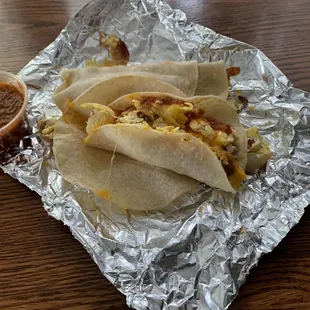 Two breakfast tacos on corn tortillas: eggs, bacon, potatoes, cheese